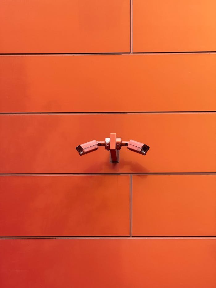Two CCTV cameras mounted on a vibrant orange wall, showcasing modern surveillance.