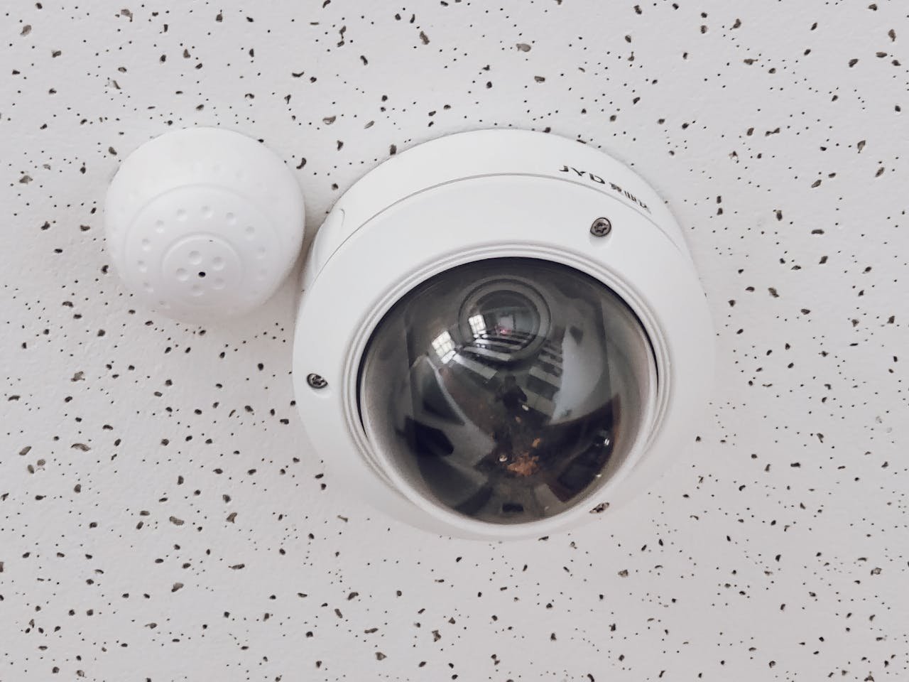 Close-up of a round dome surveillance camera installed on a speckled ceiling for security monitoring.